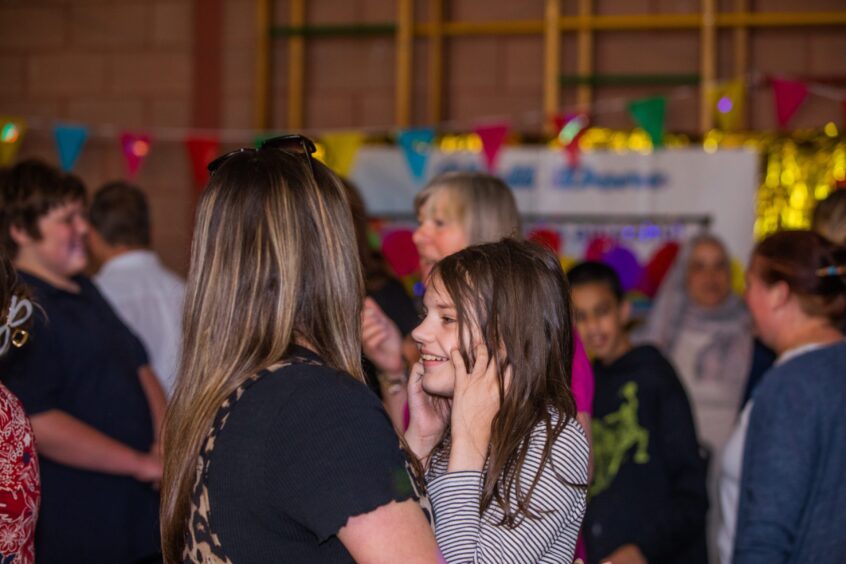 Staff and pupils dancing in a gym hall festooned with decorations. 