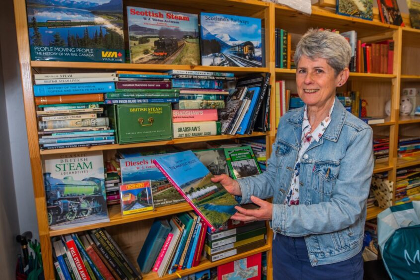 Smiling woman holding book about railways in front of shelf full of books about railways
