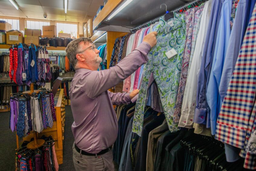 David Agnew putting colourful shifts on clothing rail in store