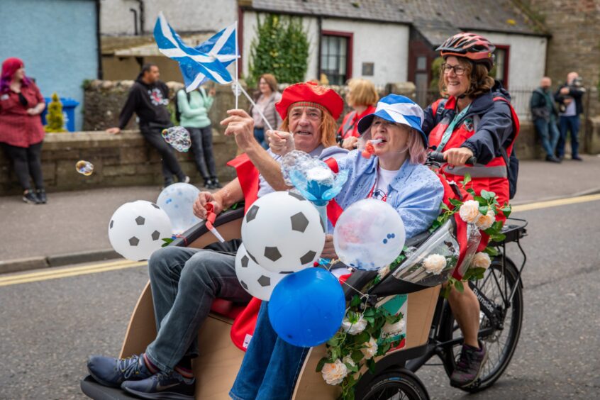 Three people waving Scotland flags on a trishaw. 