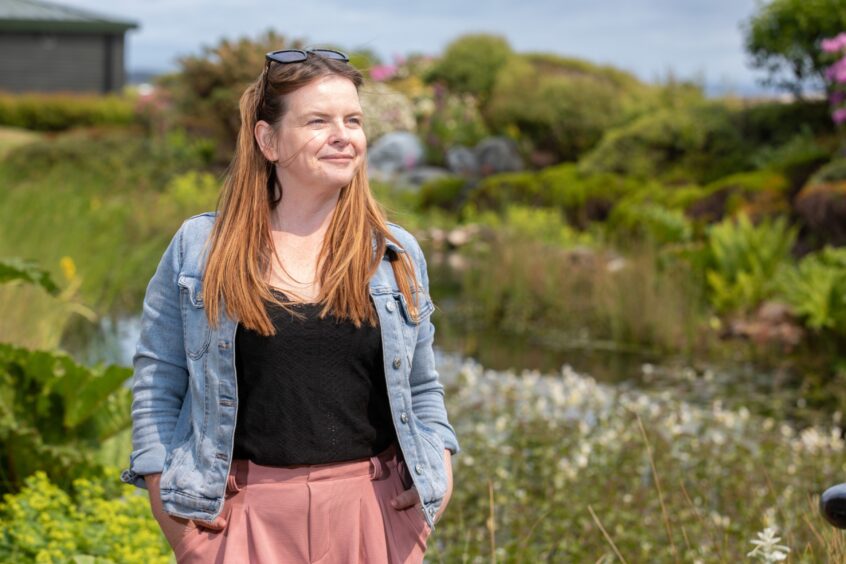 Lesley standing in a garden, smiling and looking into the distance. 