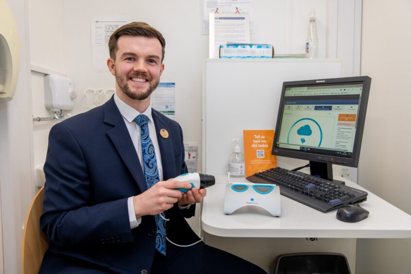 Boots pharmacist Andrew Geekie sitting at a computer and holding a mole-scanning device. 