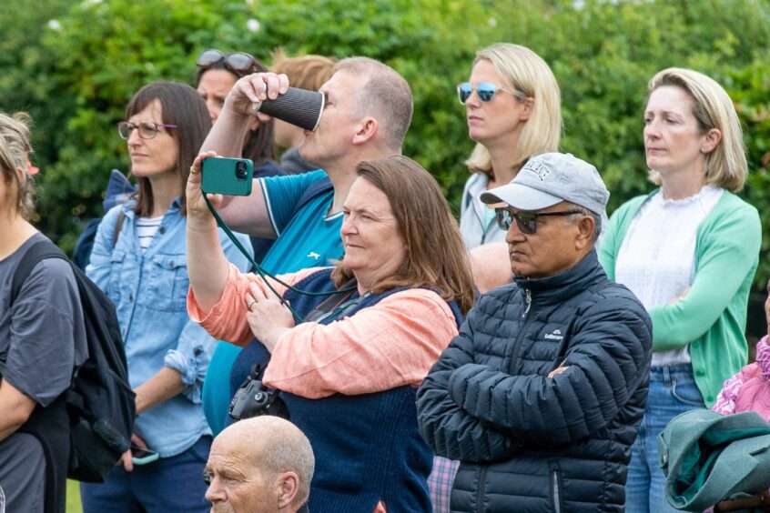 Spectators watch from the sides as one woman captures the action on her phone.