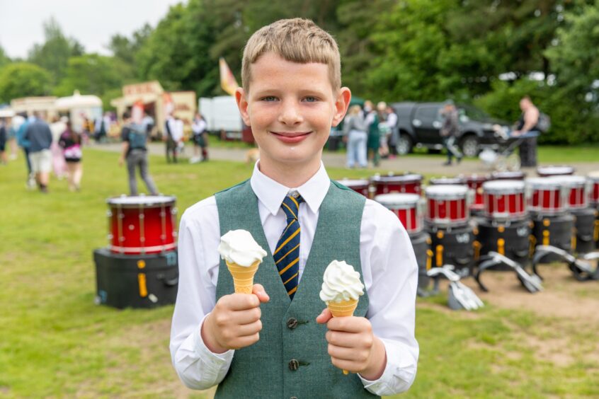 A boy in a High School of Dundee Pipe Band uniform holds two ice-cream cones.