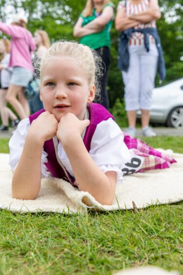 A girl in a pink Highland dancing uniform lies on her front on a blanket watching the action.