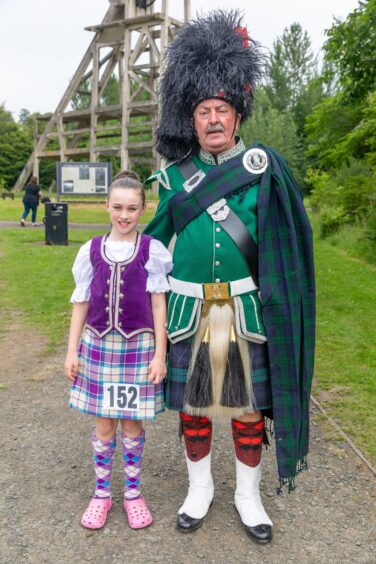 Ellie Farrell is dressed in purple Highland dancing gear while Stewart Gaughan is in full Highland dress, including a feather bonnet.