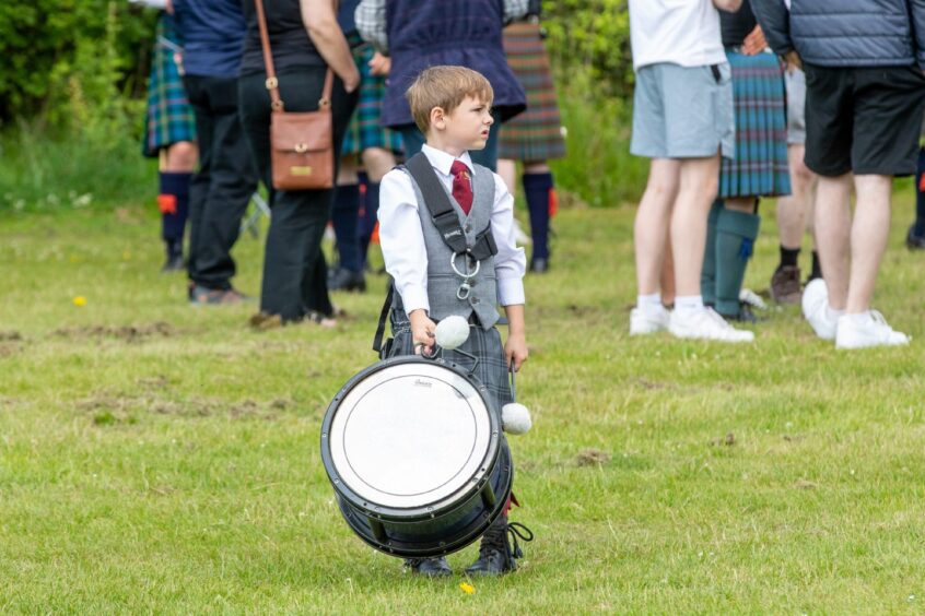 A small boy with a big drum stands in the field looking lost.