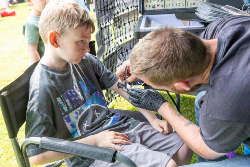 A boy gets an airbrush tattoo on his left forearm.
