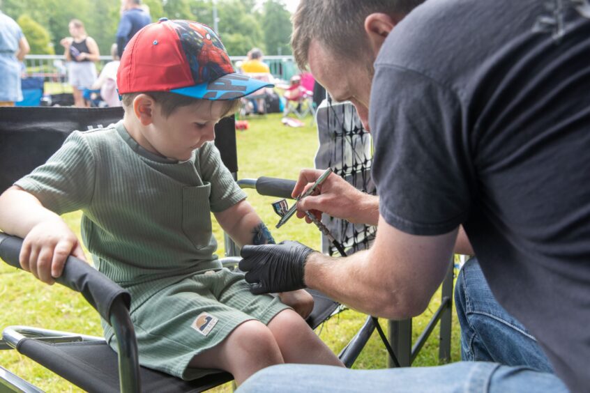A small boy is given an airbrush tattoo on his left forearm.