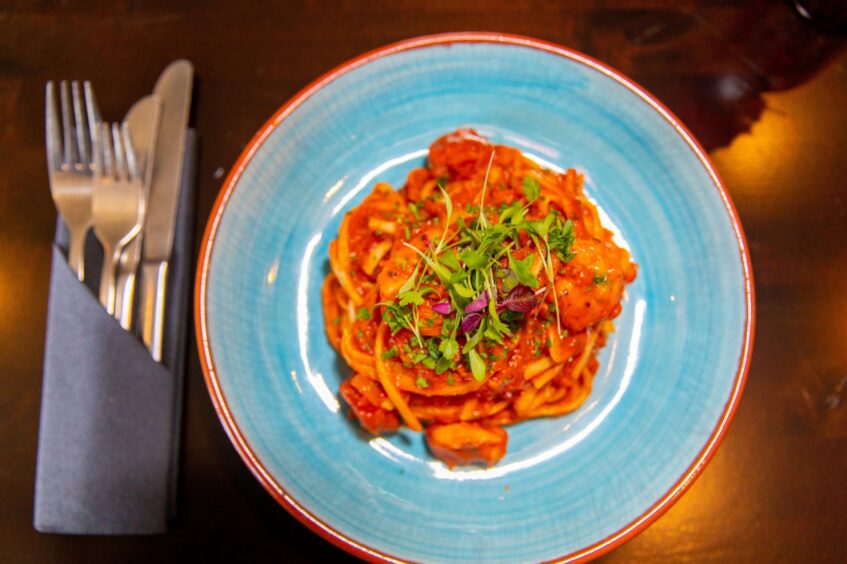 A pale blue plate of linguine in a seafood and tomato sauce piled up neatly from Porters. 