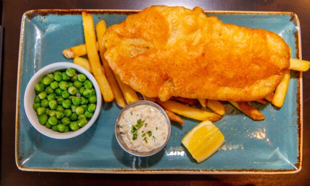 A rectangular blue plate of fish a chips with peas and tartar sauce in small bowls and a wedge of lemon,