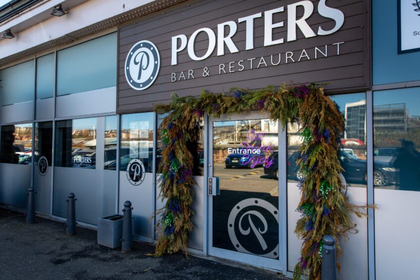 An exterior shot of Porters restaurant which has a large white sign on a brown fake wood background above a large glass door which is framed with fake foliage.