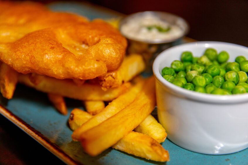 A close-up of a plate of fish and chips with peas and tartar sauce.