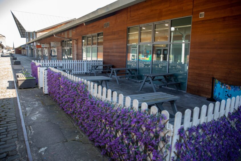 An outdoor seating area surrounded by fake purple flowers that decorate a white fence.