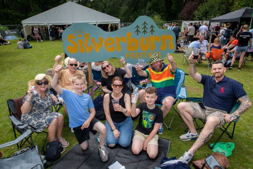 The Anderson, Predergrast and Henderson families give thumbs-up in front of the Silverburn festival sign.