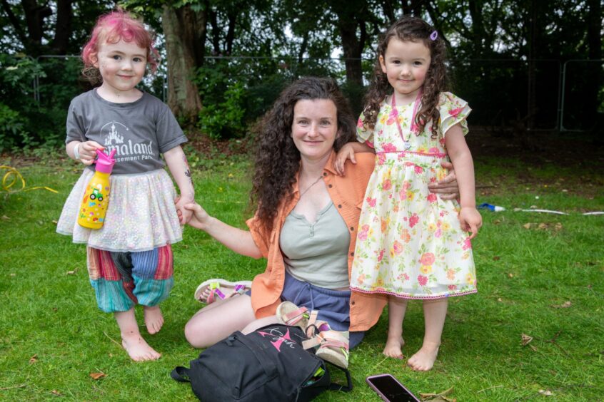 Mum Terri with Elowen (3) and Xayah (4). Terri is sitting on the grass. All three are smiling.