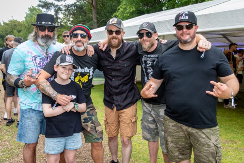 Buzzards of Babylon band members Rab, Mike, Craig, Stevie and Eck, with daughter Caitlin (8) from Kirkcaldy. They are posing with their arms around each other. Two of the men are making 'rock on' signs.