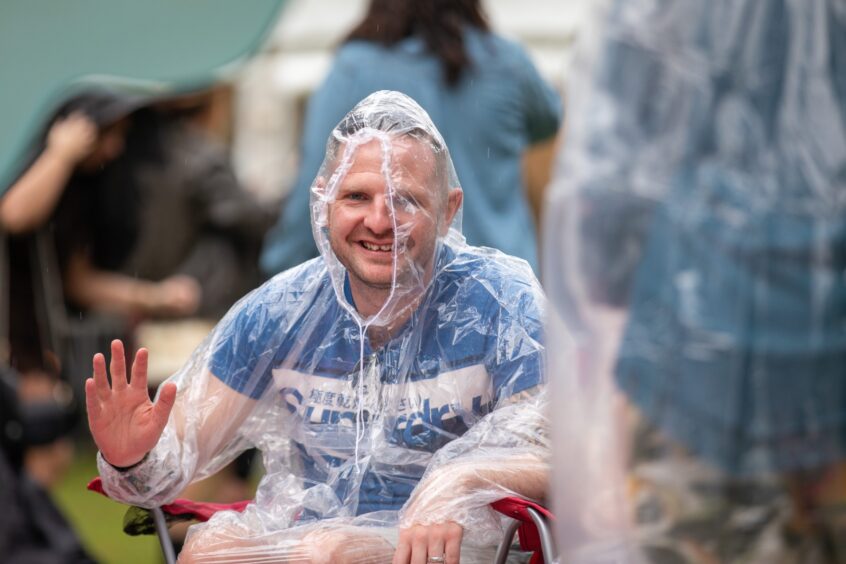 A man in a clear rain poncho smiles and waves.