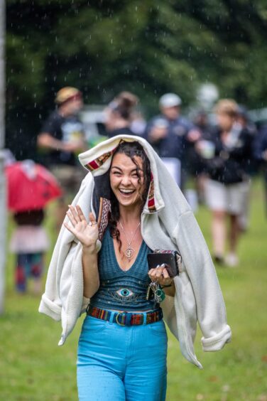 A woman smiles and waves with her jacket over her head as the rain falls.