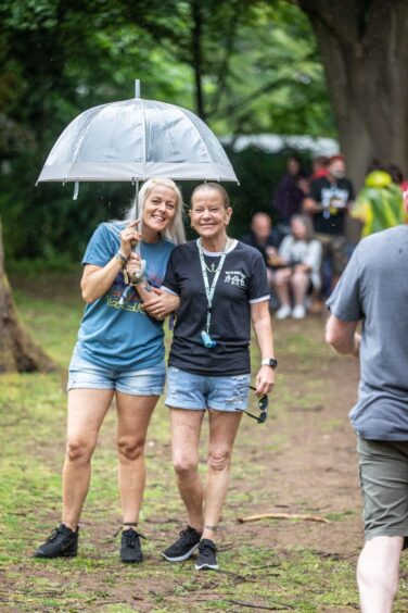 Two women shelter from the rain under a clear umbrella.