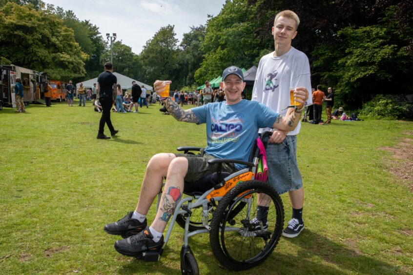 Wheelchair user Pete Simpson carries two drinks while son Ronin Simpson pushes his chair.