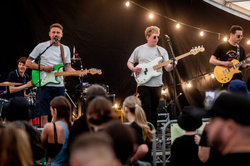 Band 'Tonto' play to a large crowd. There are two guitarists, a bassist and a drummer.