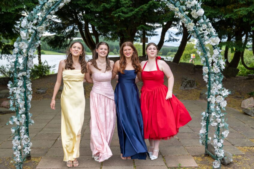 Four girls in dresses standing under an arch decorated with flowers. 