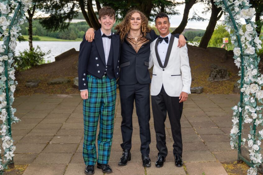 Three smartly dressed boys standing under an arch decorated with flowers. 
