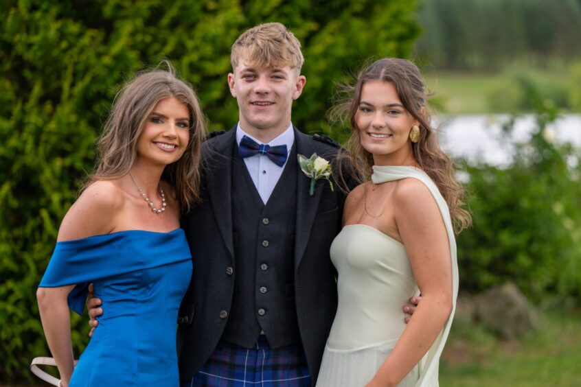 A smartly dressed boy flanked on either side by two elegantly dressed girls. 