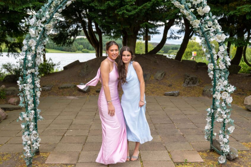 Two girls in dresses standing under an arch decorated with flowers. 