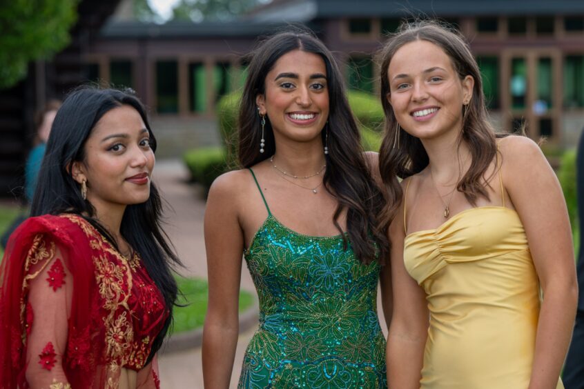 Three girls in dresses smiling outside. 
