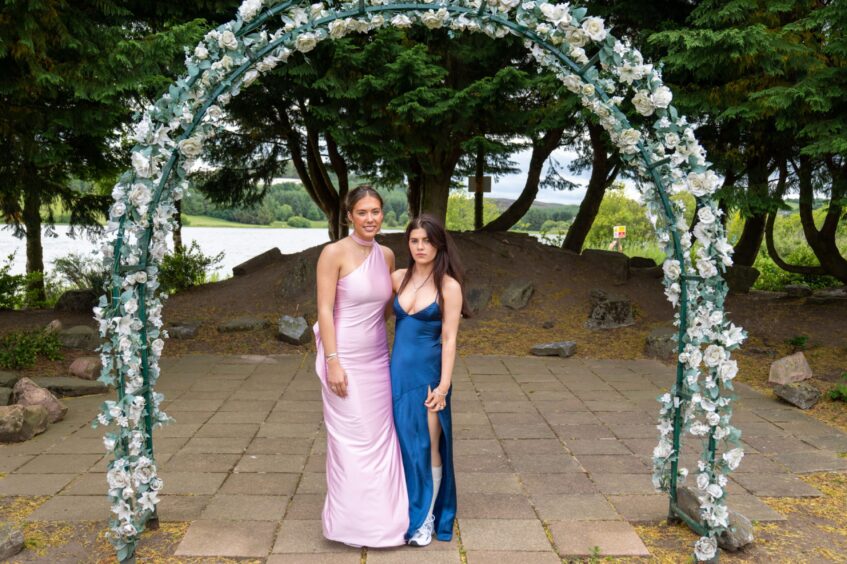 Two girls in dresses standing under an arch decorated with flowers. 