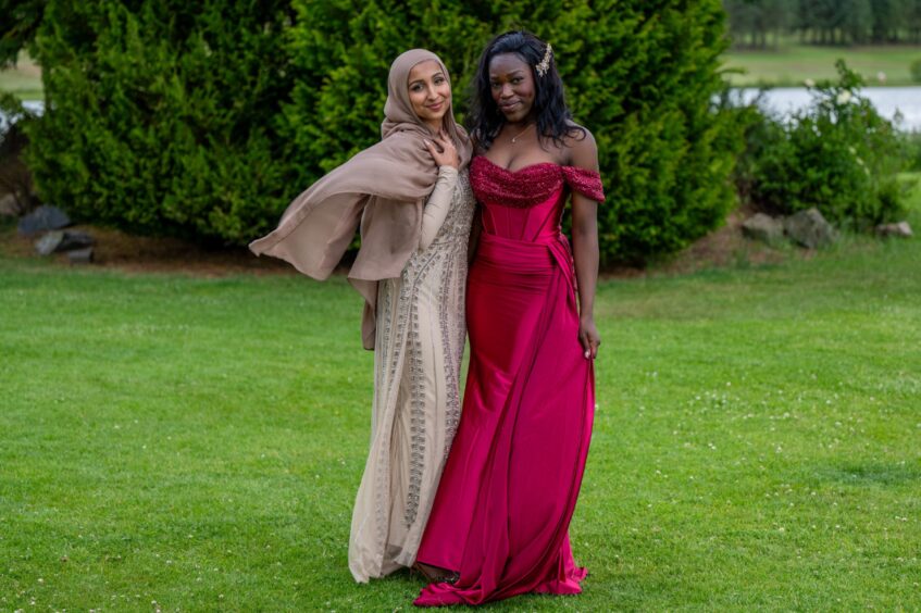 Two elegantly dressed girls pose on a lawn. 