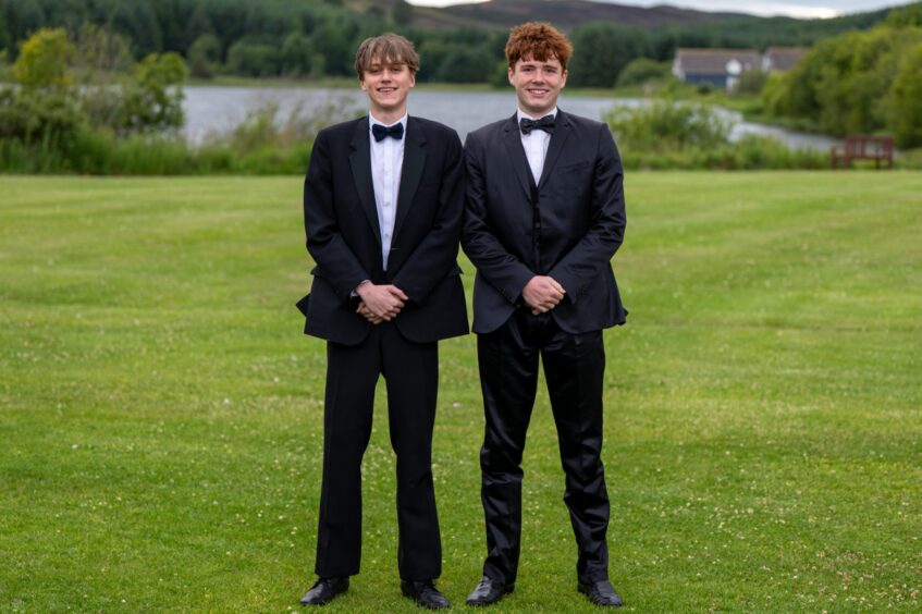 Two boys in dinner suits standing on a lawn with Piperdam Loch behind them. 