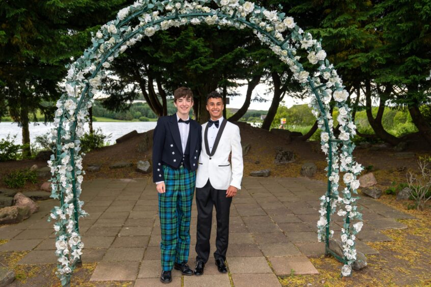 Two smartly dressed boys standing under an arch decorated with flowers. 