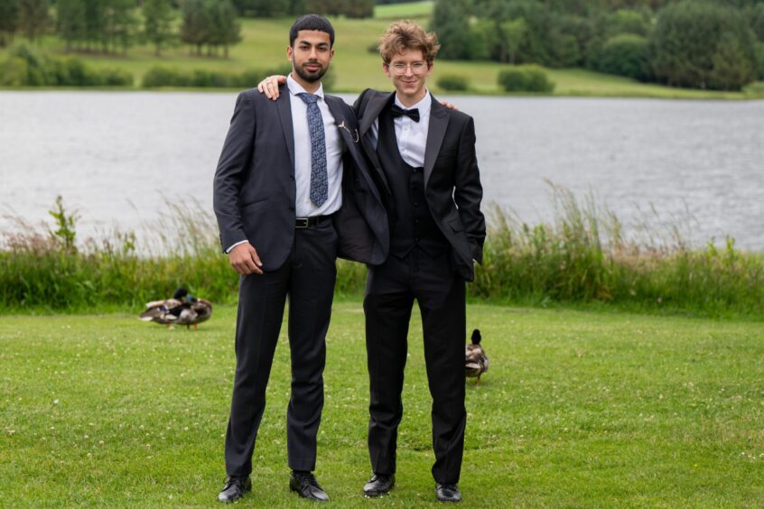 Two boys in dinner suits standing on a lawn with Piperdam Loch behind them. 