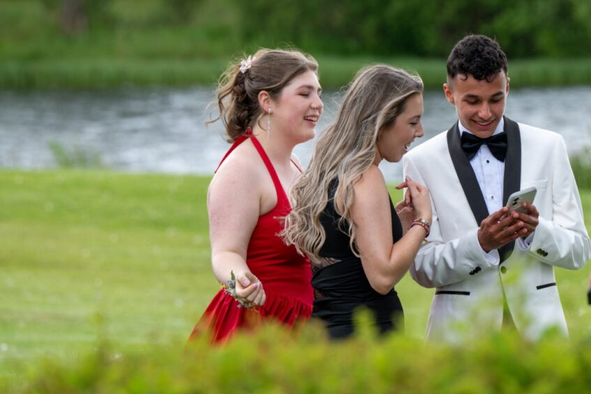 Two girls and a boy smile as they check a photo the boy has taken on his camera. 