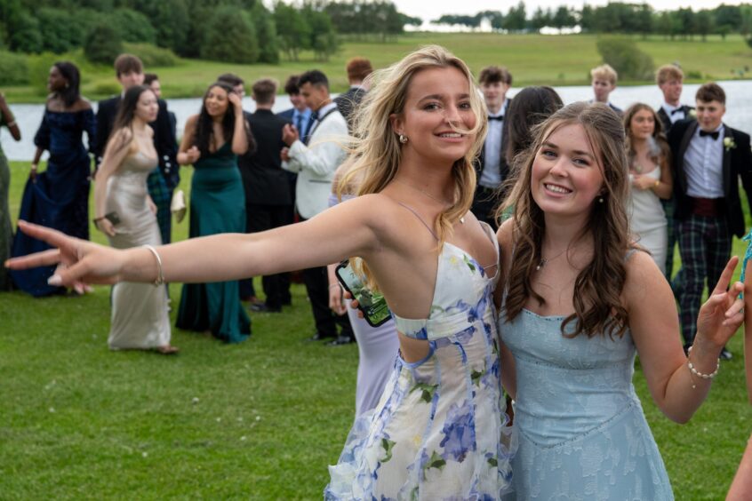 Two girls pose with other leavers behind them. 