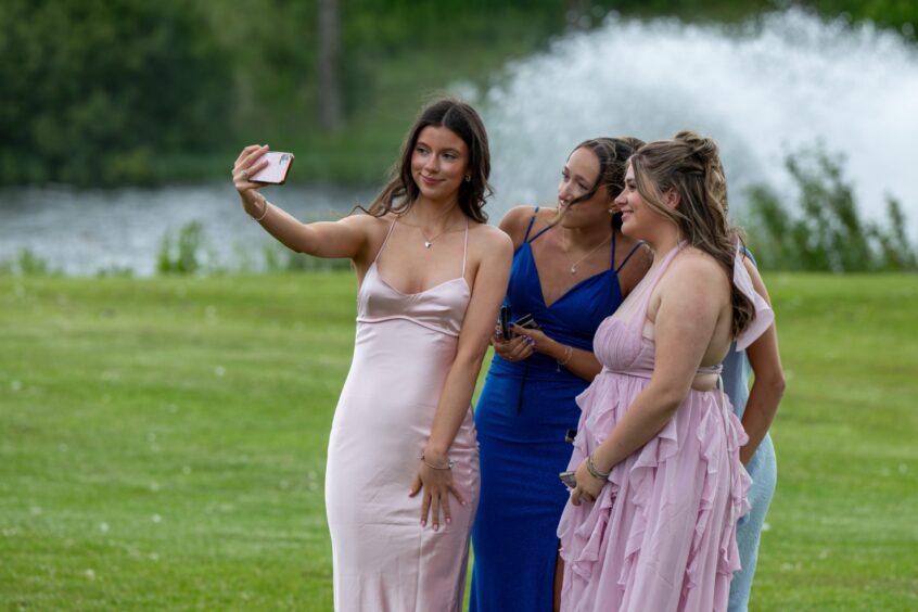 A girl takes a selfie of her and her friends outside. 