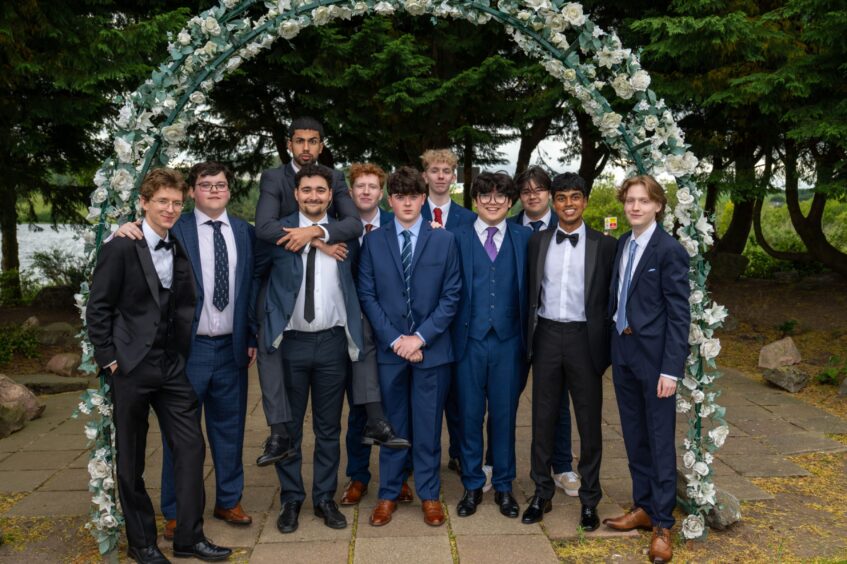 A group of boys in suits standing under an arch decorated with flowers. 