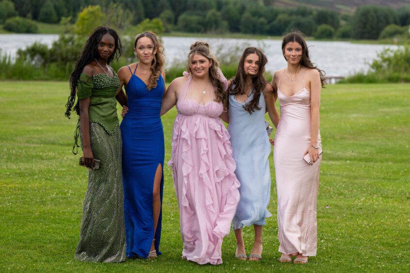 Five girls in dresses standing on a lawn with Piperdam Loch behind them. 