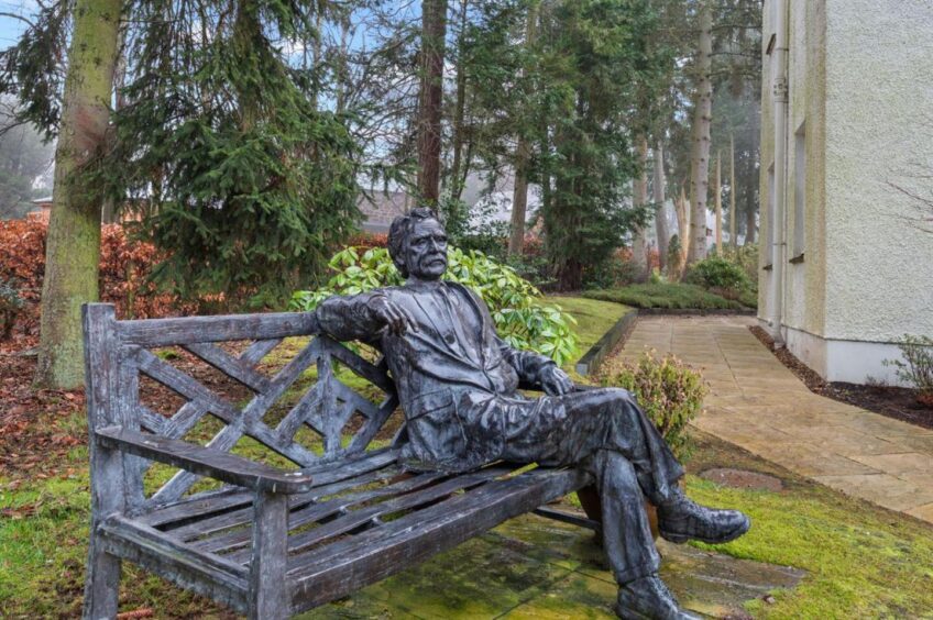 A bench with a statue in the grounds