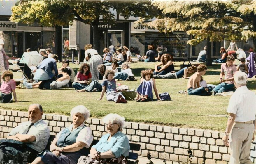 People sit on the grass and on benches, enjoying the sunshine. 