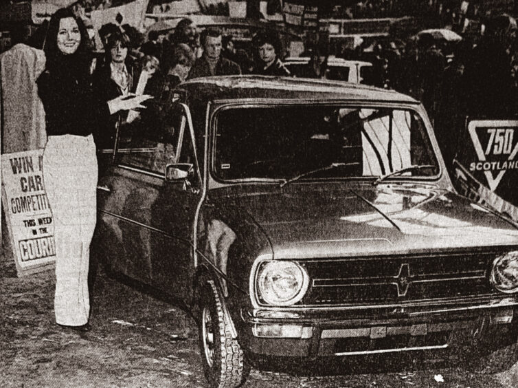 Miss Dundee Elaine Ruse stands beside the competition car, with visitors in the background. 
