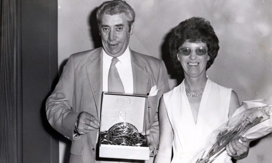 Alan and Betty Howie. She is holding flowers and he is holding a gift of a quaich in a box