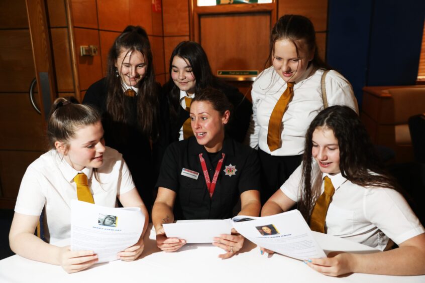 Seated at a table as the girls gather around, firefighter Jen Thomson speaks to pupils from Craigie High about her job.