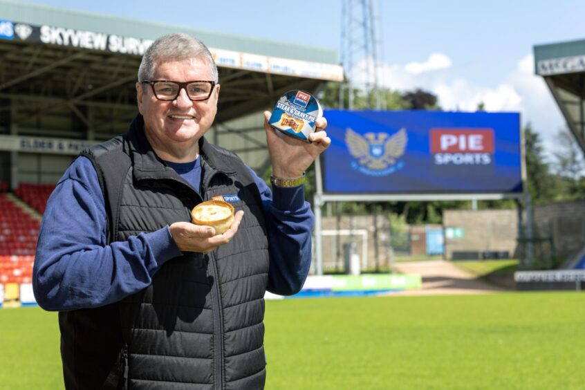 Joe Aitken holding a pie in each hand in front of the McDiarmid Park scoreboard.