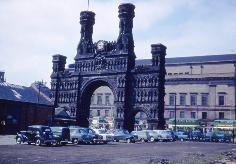 cars and buses parked by The Royal Arch in April 1963