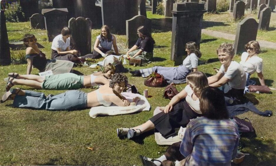 Sunbathers enjoying the hot weather in The Howff, sitting and lying amid the gravestones.