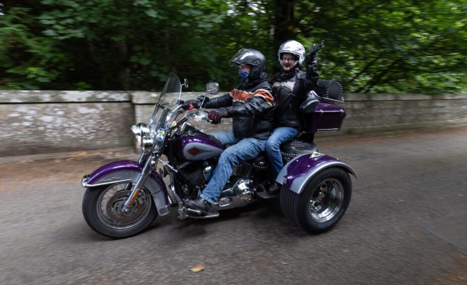 Smiling passenger waves from the back of a purple Harley-Davidson trike during the 2025 Brechin Bike and Trike Fest rideout in Angus.
